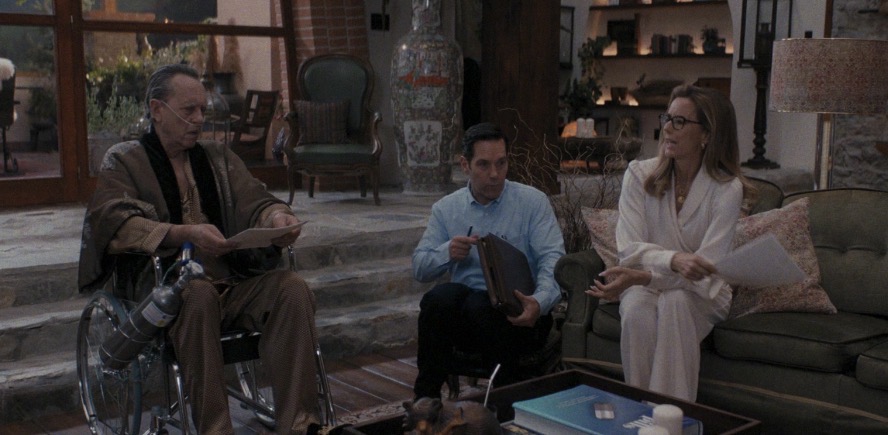 One white man sits between a wealthy white man in a wheelchair and his rich white wife.