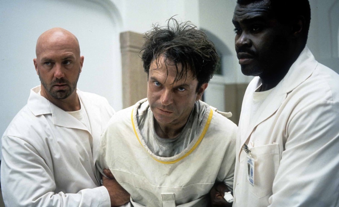 In The Mouth Of Madness: Sam Neill in a straight jacket being carried by two attendants